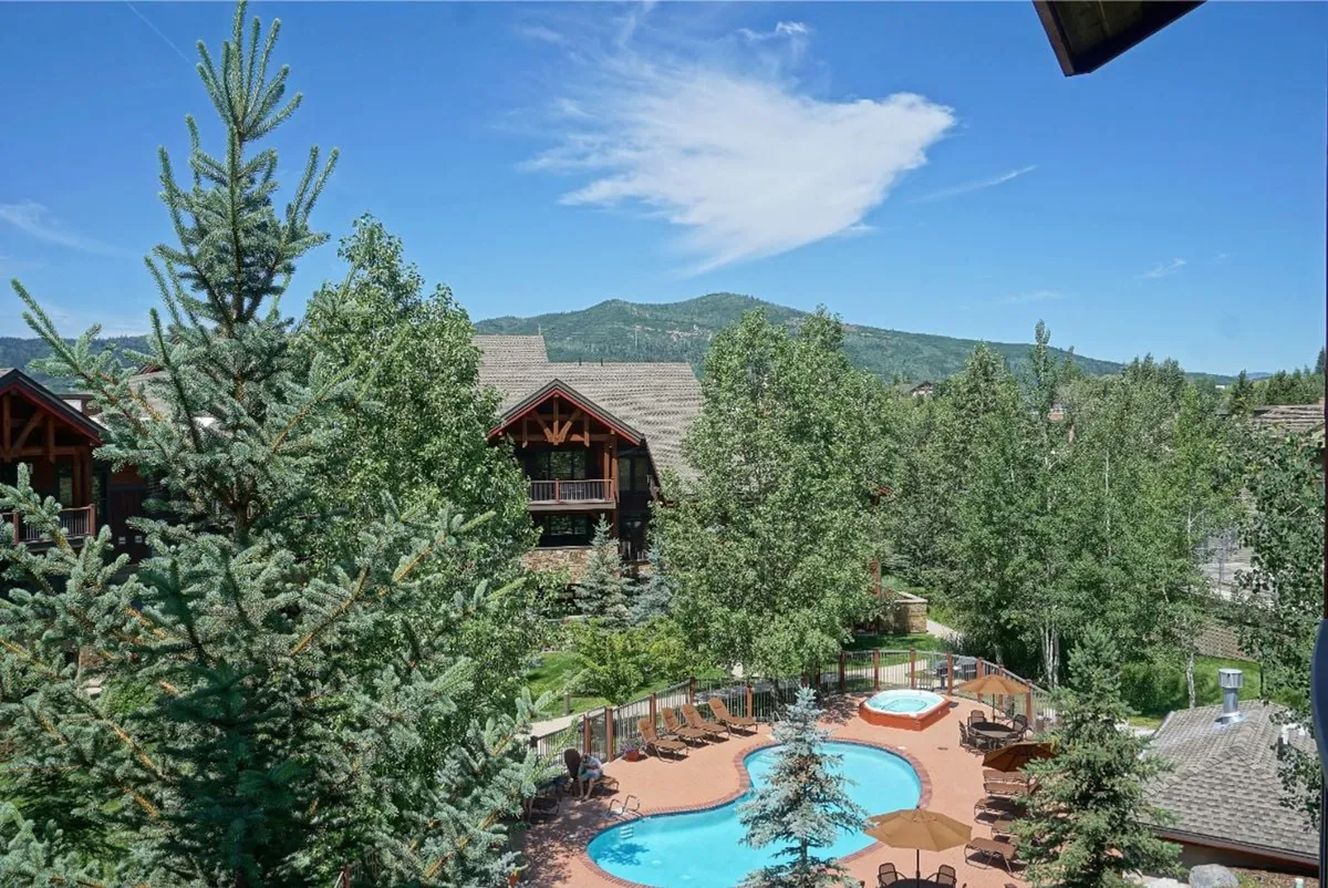 This exterior shot centers on a beautiful swimming pool framed by surrounding trees and a dramatic mountain backdrop, with hints of sunset light reflecting on the area, creating an inviting and tranquil atmosphere for outdoor relaxation.