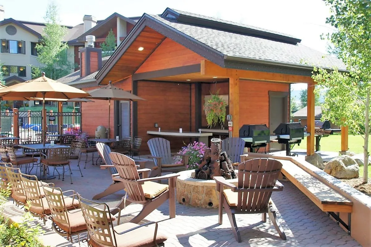 This exterior image features an outdoor seating area with a fire pit, barbecue grills, and a wooden bar structure, creating a lively setting ideal for socializing, cooking, and group events. The arrangement encourages group gatherings—perfect for both summer socials and Après Ski events.