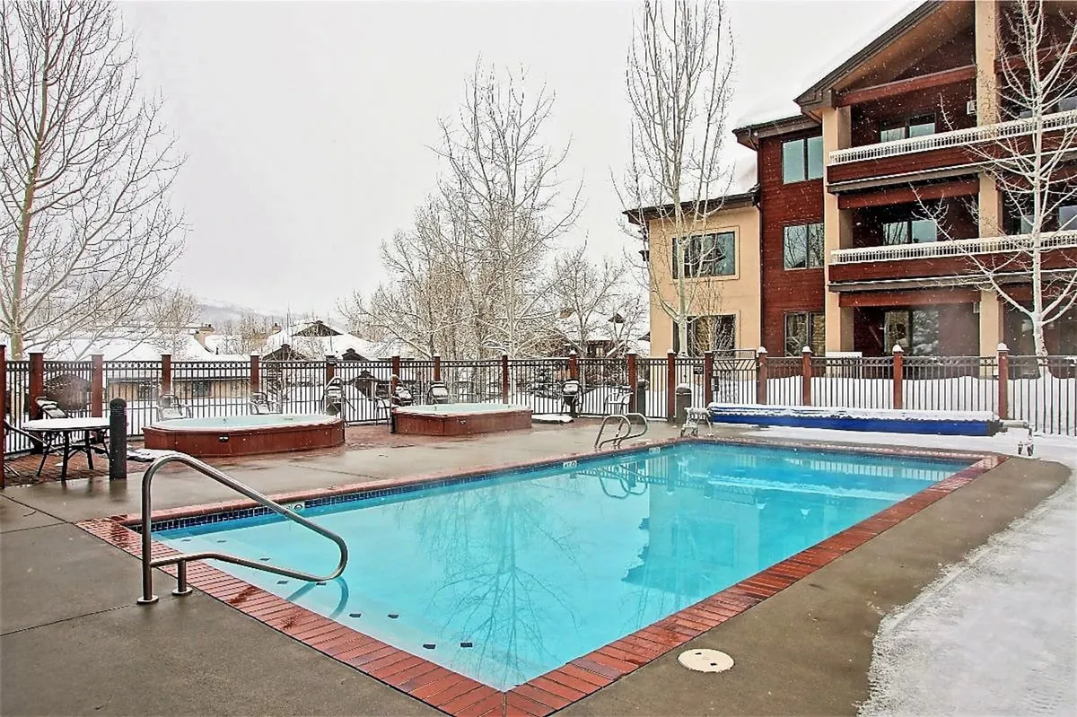 This exterior image shows a large swimming pool and multiple hot tubs surrounded by snow-covered trees and the resort buildings, capturing the inviting atmosphere of the resort’s outdoor amenities in a winter setting.