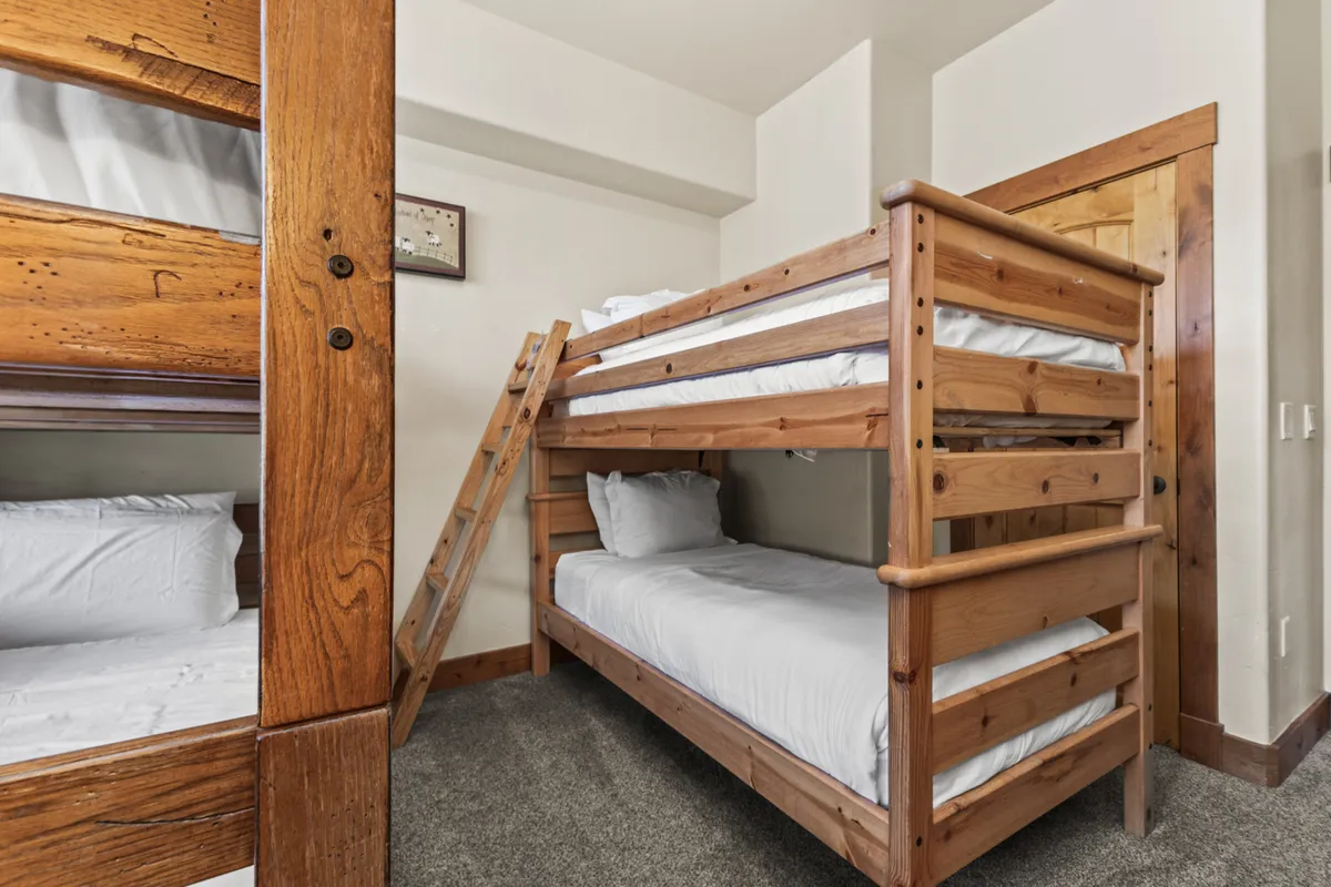 This image showcases a dedicated bunk room featuring four twin beds, a sturdy wooden ladder, and playful wall art. The room exudes a family-friendly atmosphere, inviting memories of giggles, bedtime stories, and sleepover fun.