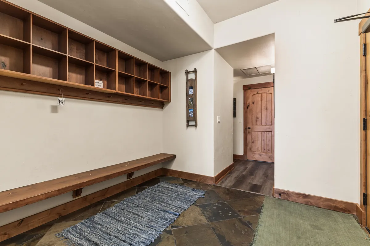 A mudroom or entryway scene with a wooden bench, open shelving for outdoor gear, a mirror, and a doorway. This space is bright and functional, ideal for coming and going with ease.