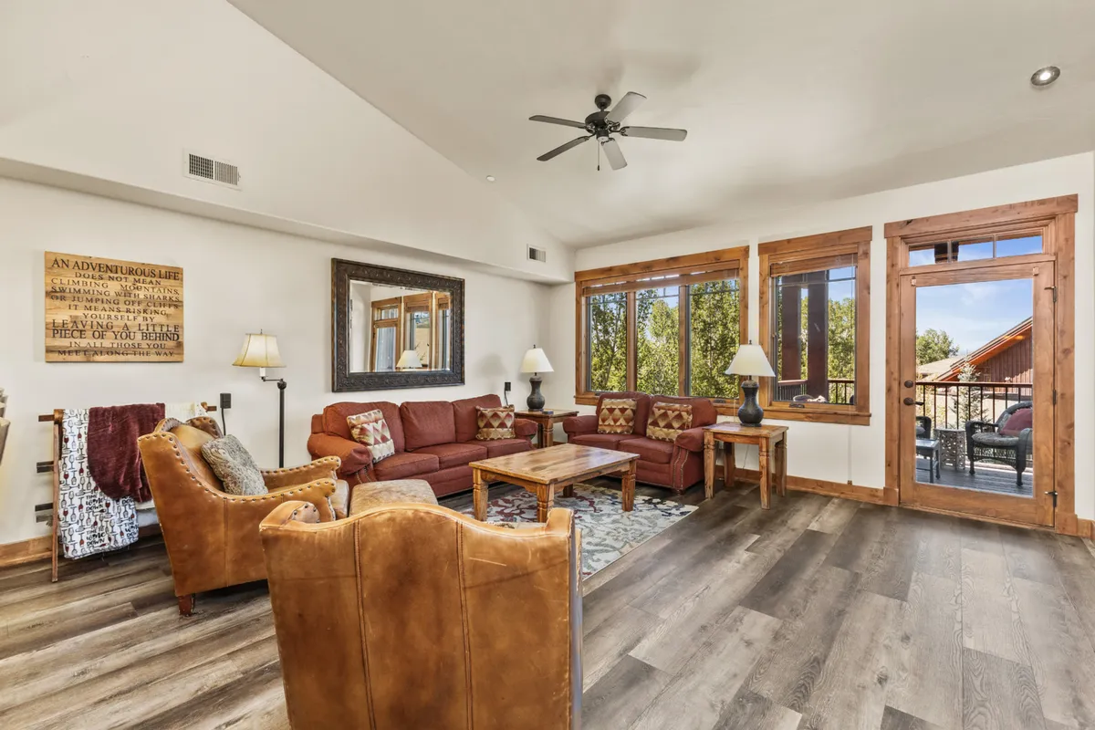 A comfortable seating area arranged around a wooden coffee table, with large windows providing ample natural light and views to the outside. Decorative wall art enhances the cozy atmosphere, making the space ideal for conversation, reading, or enjoying a movie night.