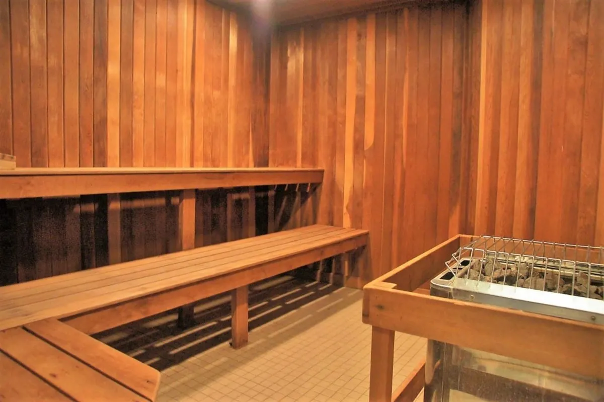 A cozy, wood-lined sauna interior with wooden benches and a sauna heater, inviting guests to relax and unwind. The warm tones, subtle lighting, and steam rising from the stones evoke a sense of comfort, wellness, and post-activity rejuvenation.