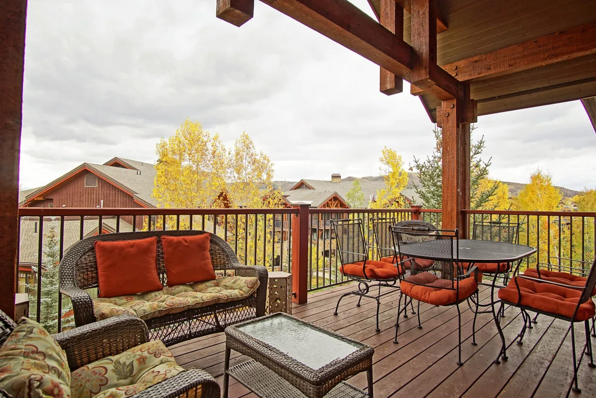 A cozy, tranquil outdoor seating area composed of wicker chairs and a glass table, framed by vibrant autumn foliage and a panoramic mountain view. The space is inviting for both quiet moments and small social gatherings, with the beauty of nature on full display.