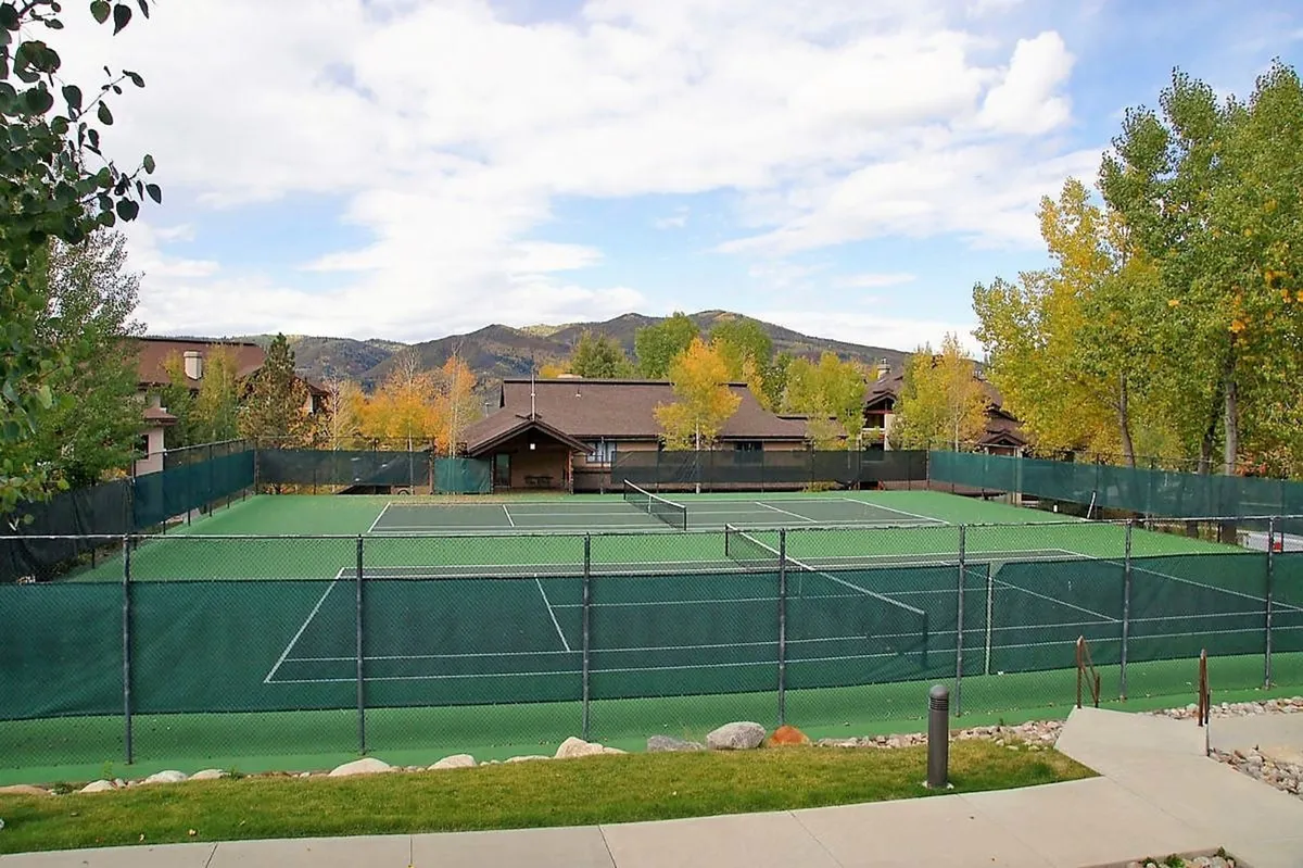 A vibrant exterior view of tennis courts framed by tall trees with mountains in the distance. The courts are ready for action, inviting guests to engage in energetic recreation against a beautiful natural backdrop.