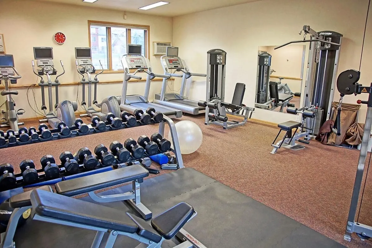 A bright, well-equipped fitness center filled with treadmills, weight machines, dumbbells, and exercise balls. The space is clean, modern, and motivational, with mirrors reflecting the active energy of the room. Some guests are seen working out, conveying a sense of health and vitality.