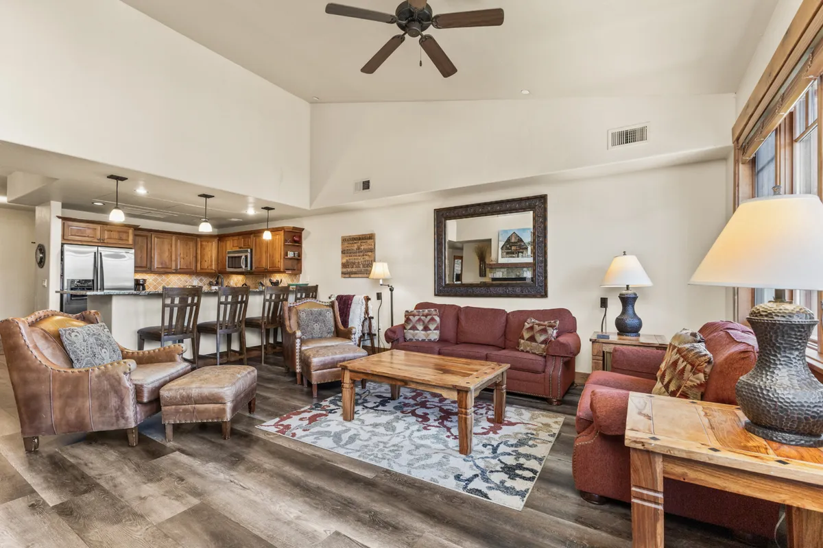This image features a welcoming living space with a wooden coffee table, comfortable seating, and a large mirror that reflects the light from the nearby kitchen bar area. The open layout hints at the home’s social nature and offers a glimpse toward the communal spaces guests might pass through before heading out.